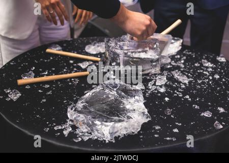 Processo di rottura del ghiaccio con martello e raccogli ghiaccio, gruppo di persone che distruggono il cubo di ghiaccio frantumato, concetto di successo del lavoro di squadra, concetto di partenza pari Foto Stock