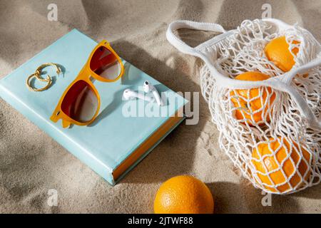 borsa di arance, auricolari e occhiali da sole sulla spiaggia Foto Stock