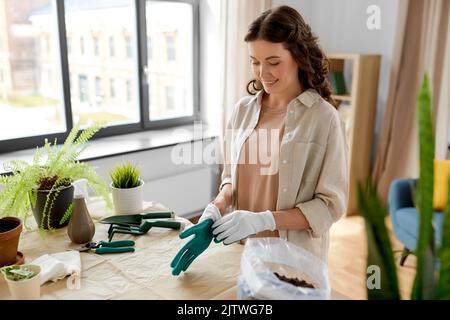 donna felice con guanti che piantano fiori a casa Foto Stock