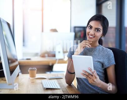 Il tablet è uno dei miei strumenti aziendali preferiti. Ritratto di una giovane donna d'affari che utilizza un tablet digitale alla sua scrivania. Foto Stock