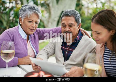 Capire i punti più fini dei social media. Un uomo anziano che mostra qualcosa alla sua famiglia sul suo tablet mentre pranzano fuori. Foto Stock