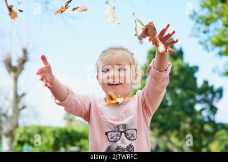 Tutto è divertente quando youre giovane. Una bambina cute che lancia lascia nell'aria mentre gioca fuori. Foto Stock