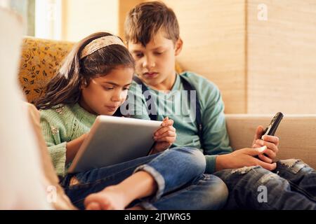 Downtime post-scuola digitale. Una bambina che usa un tablet digitale a casa mentre suo fratello la guarda. Foto Stock