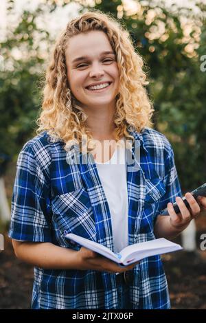 Femmina caucasica che osserva e prende nota della crescita dei frutteti di prugne. Concetto di agricoltura e tecnologia wireless. Agricoltore intelligente Foto Stock