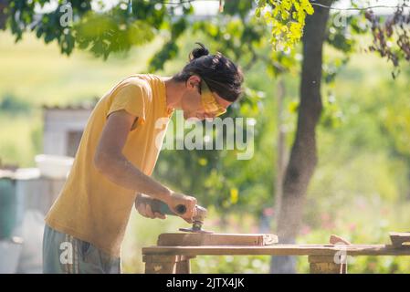 Primo piano della levigatura di un legno con levigatrice orbitale presso la carteggiatrice elettrica dell'officina che raffina la superficie Foto Stock