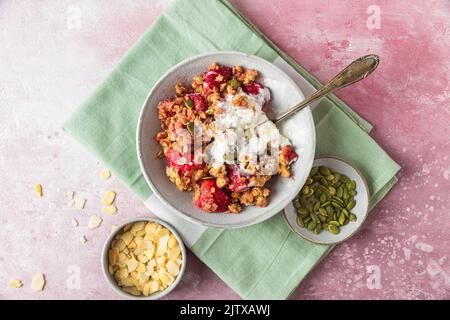Fragola crumble con gelato e mandorle in un piatto con cucchiaio su tovagliolo verde su sfondo rosa. Vista dall'alto. Colazione gustosa. Cibo delizioso Foto Stock