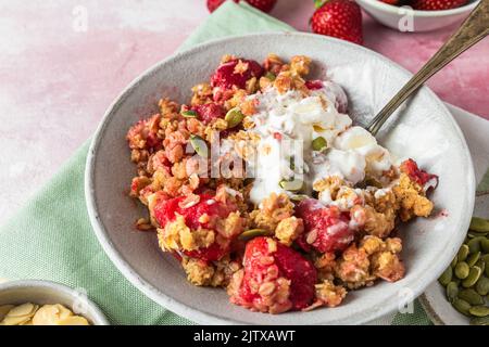 Fragola crumble con gelato e mandorle in un piatto con cucchiaio su tovagliolo verde su sfondo rosa. Gustosa colazione. Cibo delizioso Foto Stock