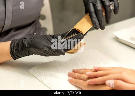 Il maestro di manicure prende gli attrezzi di manicure da una busta di kraft in un salone delle unghie Foto Stock