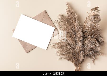 Biglietto d'auguri vuoto con canne secche o erba di pampas su sfondo beige. Giacitura piatta. Beffa. Autunno sfondo. Vista dall'alto Foto Stock