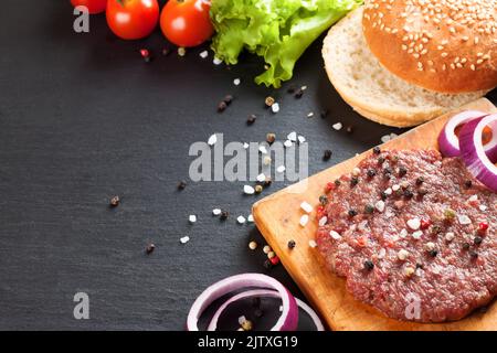 Gli ingredienti crudi per l'hamburger fatto in casa su sfondo nero ardesia con spazio copia. Foto Stock