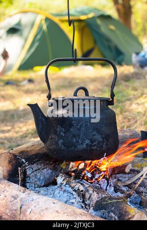 bollitore turistico affumicato sopra il fuoco del campo. Processo di cottura sulla natura. Foto Stock