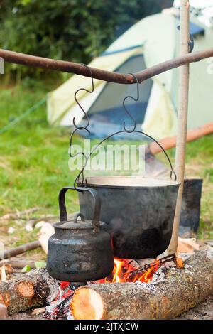 Due bollitori da turismo fumati sopra il fuoco del campo. Processo di cottura sulla natura su fondo tenda da campeggio. Foto Stock