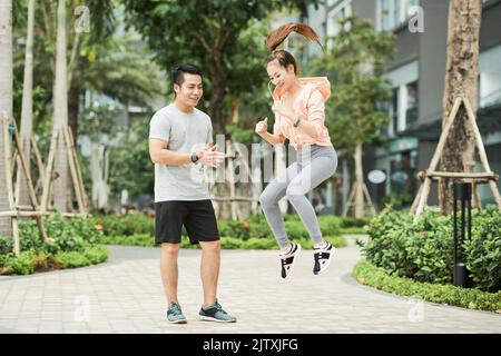 Giovane uomo asiatico che controlla come giovane donna che salta all'aperto Foto Stock