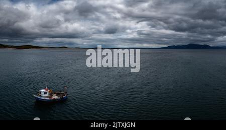 Mulranny, Irlanda - 20 luglio, 2022: Imbarcazione da pesca unica in un oceano blu profondo sotto un cielo nuvoloso con montagne costiere sullo sfondo Foto Stock