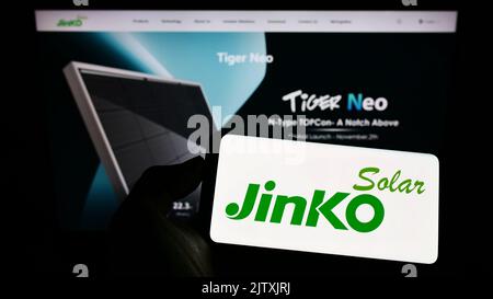 Persona che tiene il cellulare con il logo della società cinese JinkoSolar Holding Co. Ltd. Sullo schermo di fronte al sito web aziendale. Messa a fuoco sul display del telefono. Foto Stock