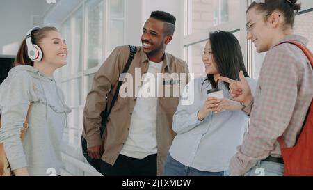 vista del gruppo multietnico di studenti che si trovano insieme nel corridoio del college. Bella ragazza caucasica è in piedi di fronte a loro spiegare e gesturing. Foto Stock