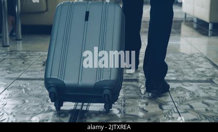 gambe di uomini d'affari che camminano attraverso la lobby dell'hotel e che tirano i bagagli e si fermano al banco della reception all'interno. Business, viaggi e persone concetto Foto Stock