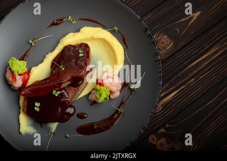 Lingue di agnello con purè di patate su un piatto, su uno sfondo di legno Foto Stock