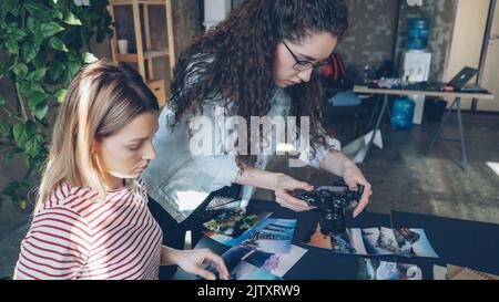 Colleghi creativi che collocano le foto sul tavolo e scattano immagini piatte mentre parlano di progettazione del progetto. Vista dall'alto del tavolo moderno con illustrazioni, notebook e pennarelli. Foto Stock