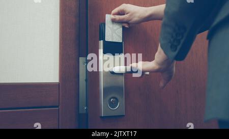 Primo piano di una donna d'affari in tuta aprire la porta della camera d'albergo usando la chiave senza contatto e entrando nella camera. Concetto di viaggi, affari e persone Foto Stock