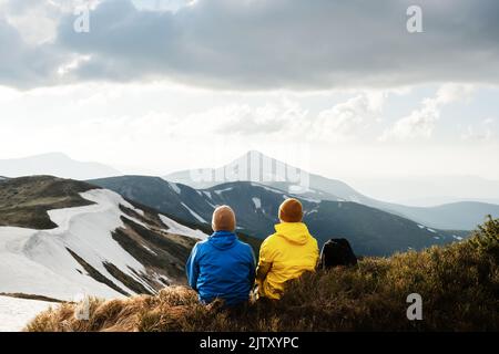 Due turisti si trovano sul bordo di una cima di montagna. Montagne nebbie sullo sfondo. Carpazi ucraini, Ucraina. Fotografia di paesaggi Foto Stock