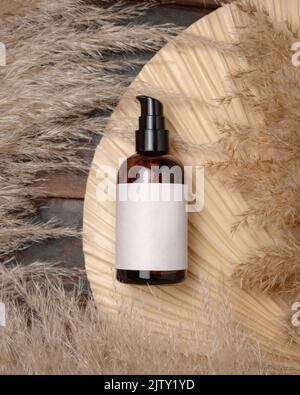 Cosmetic una bottiglia della pompa sulla foglia di palma asciutta vicino alla vista superiore dell'erba del pampas, mockup dell'etichetta. Prodotti di bellezza per la cura della pelle, lozione o essenza. Eco-friendly bohémien Foto Stock