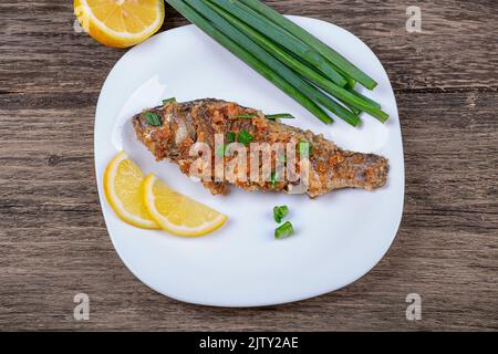 Pesce fritto impanato con cipolle verdi e limone, in un piatto su un vecchio sfondo di legno Foto Stock