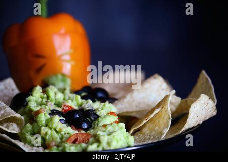 Ragni di olive nere che strisciare su guacamole con patatine fritte. Messa a fuoco selettiva su bug con primo piano e sfondo sfocati. Pepe come mostro con la fa tagliata Foto Stock