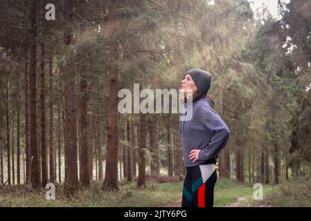 Ritratto di corridore femminile con le mani sui fianchi in una foresta, riposante dopo una corsa o un esercizio fisico. Foto Stock