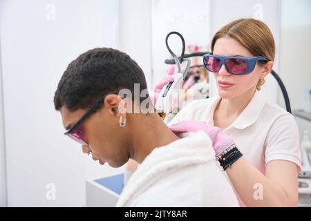 Salone di bellezza cosmetologist che esegue la rimozione dei capelli sul collo maschio del cliente Foto Stock