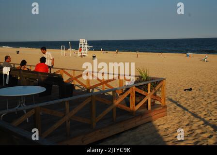 Un gruppo di fienile si siede su una panchina e ringhiera nel tardo pomeriggio come la maggior parte della spiaggia si libera in una giornata di vacanza estiva Foto Stock