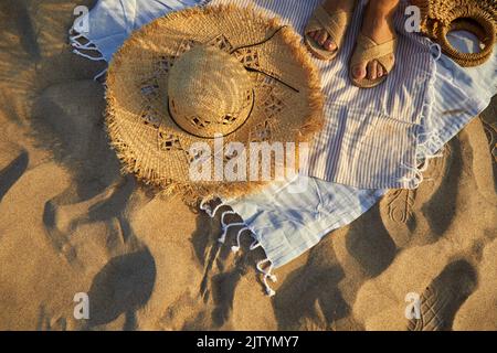 Vista dall'alto degli accessori da spiaggia. Cappello di paglia, borsa, infradito sulla sabbia in spiaggia. Foto Stock