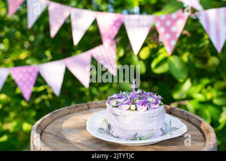 Bellissima torta bento con viola, veri peri, fiori di mattiola con foglie verdi, candele nella torta sullo sfondo di bandiere rosa. Compleanno. Foto Stock