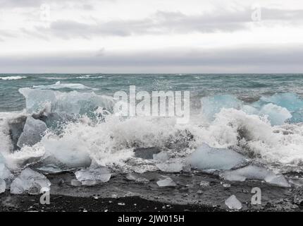 Frammenti di ghiaccio spezzati dal ghiacciaio, galleggiano verso il mare e poi si lavano sulla sabbia nera di Diamond Beach a Jökulsárlón, costa meridionale dell'Islanda. Foto Stock