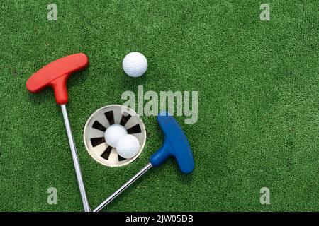 Putters e palle da golf in miniatura assortiti si inclinano su erba sintetica. Foto Stock