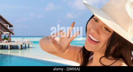 donna sorridente in cappello di paglia che mostra pace sulla spiaggia Foto Stock