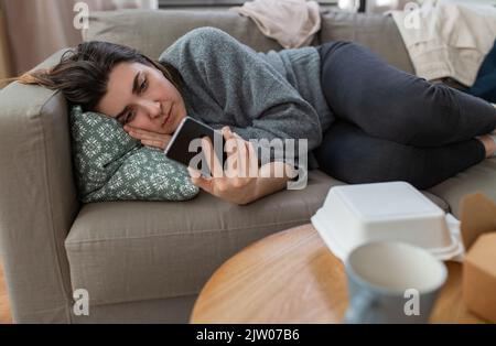 donna stressata con smartphone sul divano a casa Foto Stock