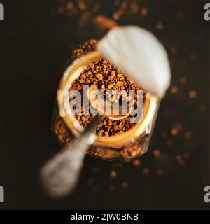 Vista dall'alto di un vasetto con caffè forte istantaneo, in cui è presente un cucchiaino da tè in argento, in piedi su uno sfondo scuro. Caffè istantaneo per colazione. Amore o Foto Stock