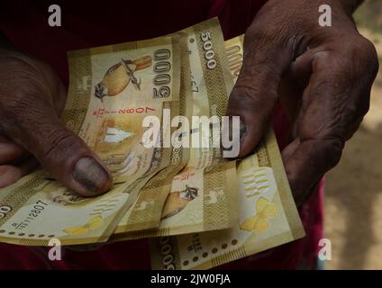 Horana,Kalutara District,Sri Lanka-Luglio 30 2022:Vista ravvicinata delle mani di una vecchia donna che conta poche banconote di rupia dello Sri Lanka 5000 Foto Stock