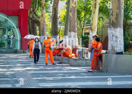 Gente cinese nelle uniformi della spazzatrice di strada. Stanno facendo una pausa fuori da una stazione della metropolitana o dal treno leggero Xi'an. Foto Stock