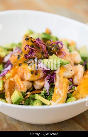 Insalata di gamberetti, avocado, cavolo rosso, lattuga, carota e frutto della passione, servita in un recipiente bianco. Foto Stock