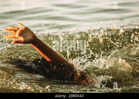 Un uomo sta annegando in acqua. Una mano sbirciata da sotto un'acqua. Una persona affogata ha bisogno di aiuto, soccorso. Un rischio, pericolo di vivere in mare, fiume, oc Foto Stock