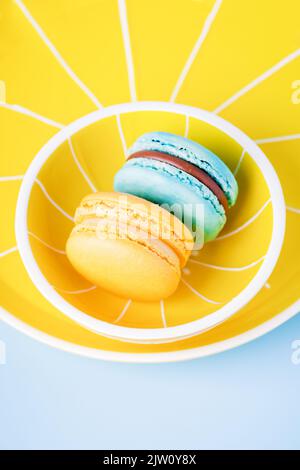 Macaron blu e giallo su piatto giallo e fondo blu Foto Stock