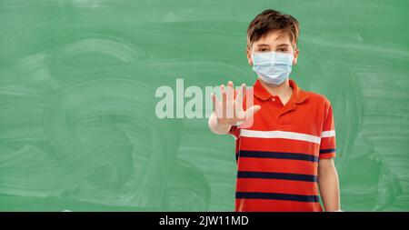 ragazzo studente in maschera medica su lavagna verde Foto Stock