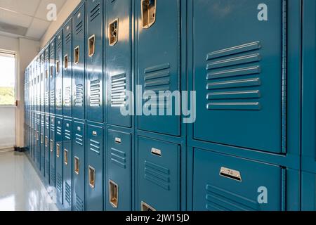 Armadietti in metallo blu lungo un corridoio non descritto in una scuola superiore tipica degli Stati Uniti. Nessuna informazione identificabile inclusa e nessuno nella sala. Foto Stock