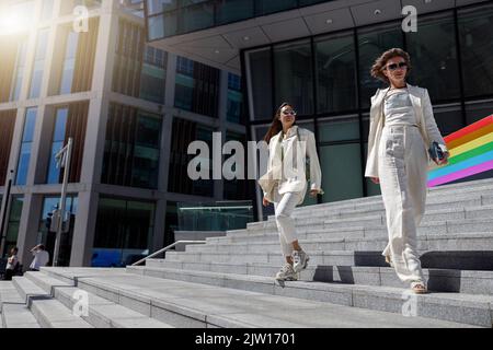 Due donne in abiti alla moda camminano all'esterno sullo sfondo di un edificio moderno Foto Stock