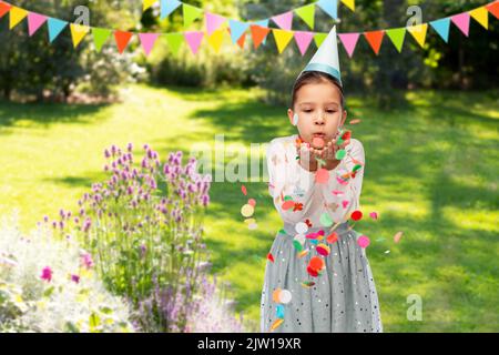 ragazza che soffia i confetti alla festa di compleanno in giardino Foto Stock