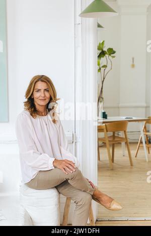 Donna d'affari matura sorridente seduta sul divano in ufficio creativo Foto Stock