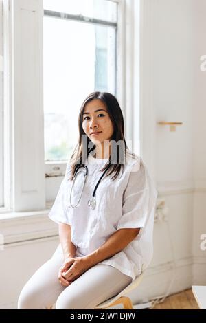 Ritratto di giovane medico fiducioso seduto in clinica Foto Stock