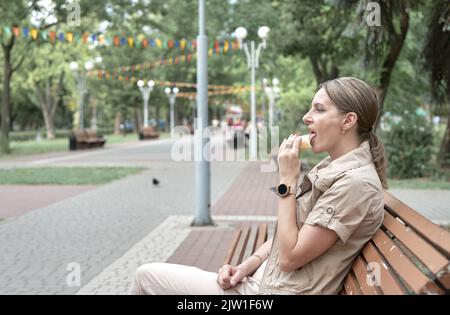 Donna di mezza età da sola riposa su panchina nel parco e mangia gelato. Foto Stock